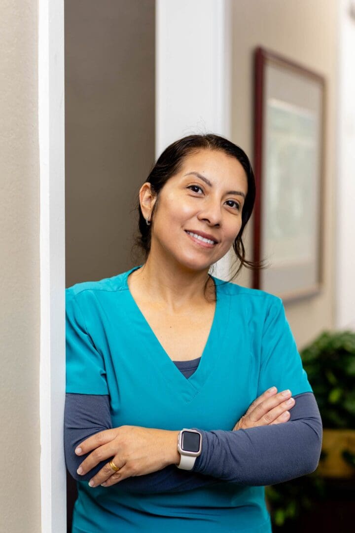 Smiling woman in blue scrubs, crossing arms.