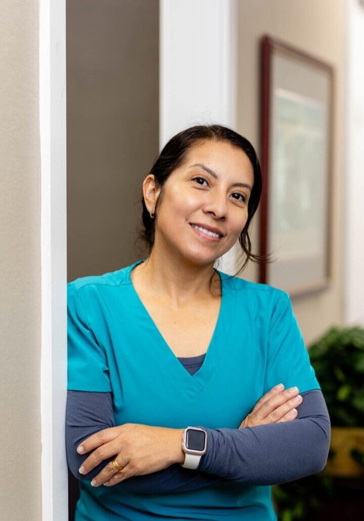 Smiling woman in blue scrubs, crossing arms.