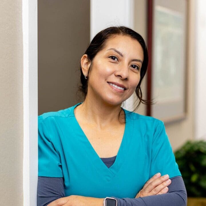Smiling woman in blue scrubs, crossing arms.